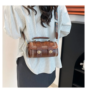 Close-up of brown cylinder crossbody bag with contrast stitching and ethnic embroidered strap