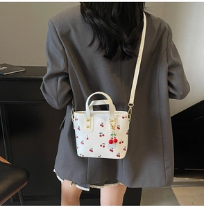 White cherry print bucket bag with 3D cherry charm shown on shoulder with casual blazer