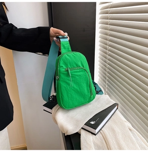 Detail of bright green nylon crossbody bag showing the zipper pocket and blue wide strap