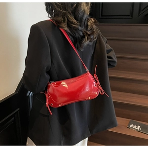 Detail of red glossy leather baguette bag featuring side bows and silver metal studs