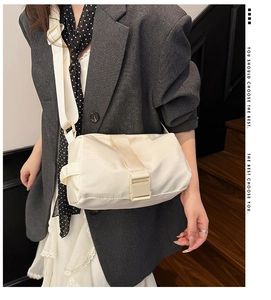 Model wearing a cream nylon crossbody toast bag with a wide strap and buckle detail