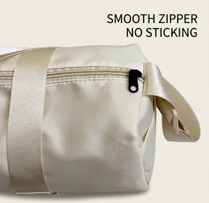 Detail of smooth metal zipper and silky nylon fabric on cream crossbody gym bag