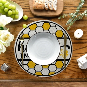 Close-up of round linen placemat with yellow bee pattern and plate on wooden table