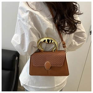 Detail of trendy small square handbag with woven flap and gold sculptural metal handle