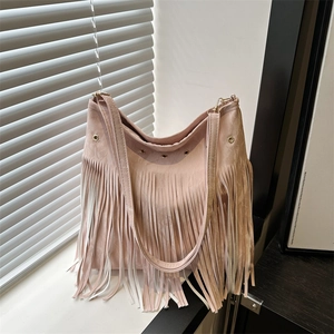Pink faux suede crossbody bag with long fringes and gold eyelets on a window sill