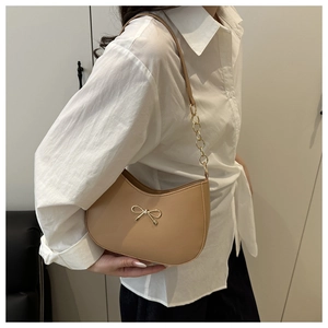 Detail showing beige crescent bag with gold bow buckle and chain strap on a white shirt