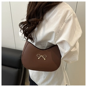 Close-up of a dark brown crescent bag with a decorative gold bow buckle on a white shirt