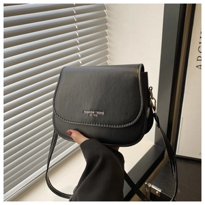 Detail of matte black saddle bag featuring silver text print and adjustable shoulder strap