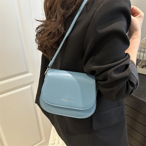 Minimalist light blue saddle bag with Fashion Trend print worn over a black blazer