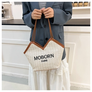Detail of woven straw tote bag with brown leather trim and MOBORN PARIS embroidery