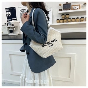 Detail of woven straw tote bag with black logo and leather straps on model's shoulder