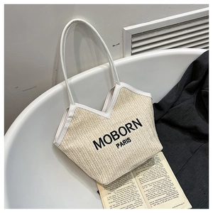 Détail du sac cabas en paille tressée avec lettrage noir et lanières en cuir blanc