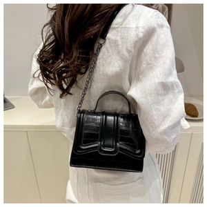 Detail of black crocodile texture handbag with chain strap shown on person