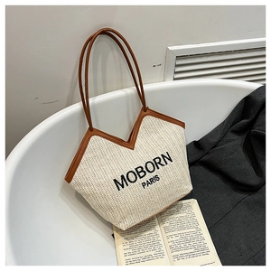 Détail du sac cabas en paille à chevrons avec poignées en cuir marron et lettrage