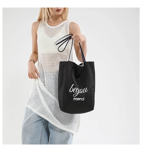 Close-up of black canvas tote bag featuring white beyou merci artistic lettering