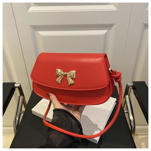 Détail d'un sac selle en cuir rouge avec une boucle nœud dorée et des détails de sangle