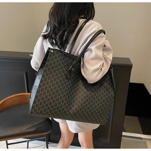Detail shot of black tote bag with M-pattern monogram showing on-shoulder fit and style