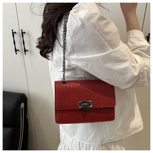 Detail of red crocodile pattern shoulder bag with black metal chain strap on model