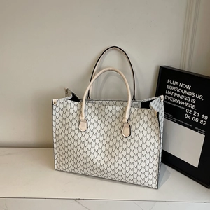 Chic beige tote bag with black letter M print and brown handles on marble surface