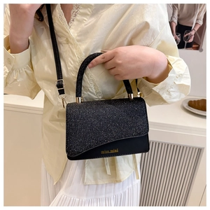Detail of black sequined handbag with gold logo, top handle, and adjustable shoulder strap