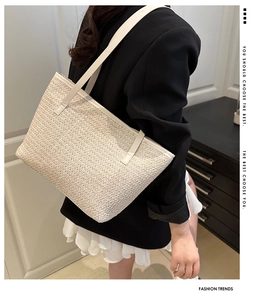 Detail of summer straw tote bag with white leather straps shown on a model in a casual setting