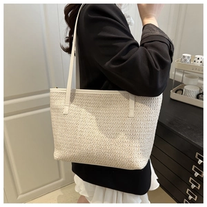 Detail of off-white woven tote bag showing fine straw texture and smooth slim shoulder straps