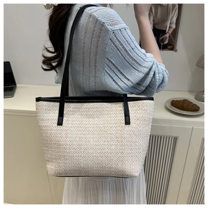Detail of a minimalist beige woven tote bag with slim black leather shoulder straps