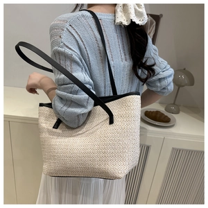 Detail of minimalist straw tote bag with black leather straps on woman's shoulder
