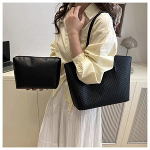 Close-up of black woven tote bag and matching clutch set shown on a female model