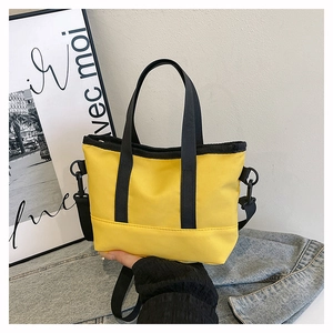 Detail view of bright yellow canvas tote with black woven handles and detachable strap