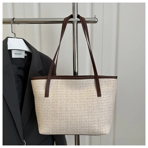 Detail of woven straw tote bag with brown leather straps hanging on a metal rack