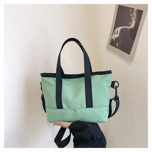 Detail of mint green canvas tote bag with black woven handles and detachable strap