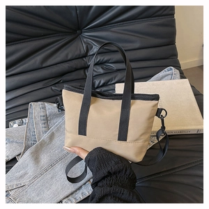 Detail of khaki canvas handbag with black straps and matte D-ring on leather surface