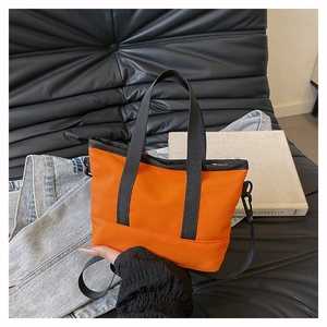 Detail of orange nylon tote bag with black canvas straps and adjustable crossbody strap