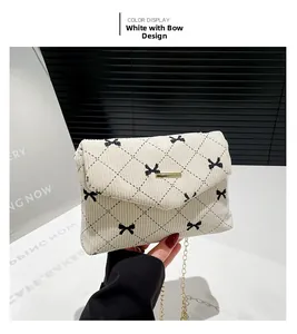 Close-up of white corduroy shoulder bag with black bow embroidery and gold metal chain