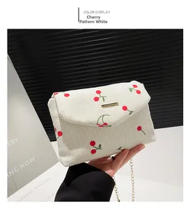 Detail of white corduroy shoulder bag with red cherry prints and golden chain strap