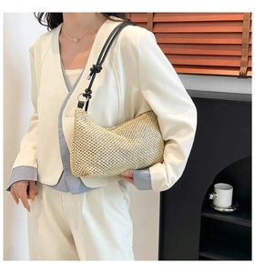 Close-up of woven straw handbag with black leather strap and metal ring detail