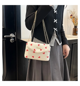 Detail of white corduroy envelope bag with red heart pattern and gold chain strap
