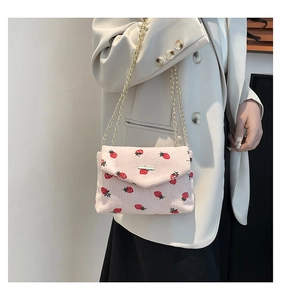 Detail of pink strawberry corduroy bag with golden chain strap on a model outfit
