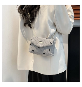 Detail of grey quilted crossbody bag with small black bows and gold chain strap