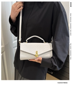 Close-up of white woven shoulder bag featuring a gold musical note swivel lock