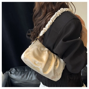 Detail of elegant cream satin shoulder bag with gold embroidery and ruffled handle