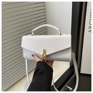 Detail of white woven texture bag with gold musical note clasp and thin shoulder strap