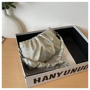 Close-up of light green satin pleated cloud bag with golden floral embroidery patterns