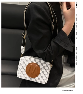 Détail du sac bandoulière blanc avec motif M gris et écusson en cuir marron sur le devant