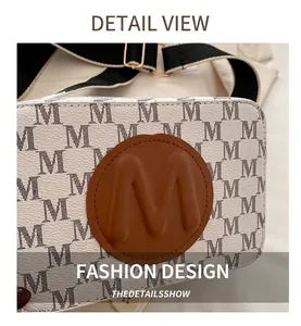 Détail du sac caméra avec motifs imprimés et écusson en cuir marron avec logo M