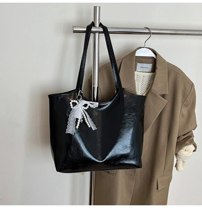 Detail of black faux leather tote bag with white lace bow and pearl charm on a metal hanger