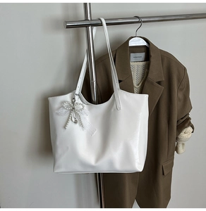 Close-up of white leather tote bag with pearl and lace bow pendant on a metal stand