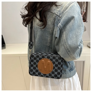 Détail du sac à bandoulière en toile monogramme avec écusson en cuir rond et large sangle