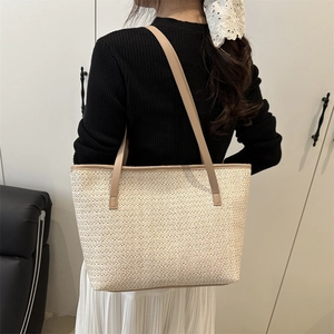 Minimalist beige straw woven tote bag with brown leather straps shown on a model